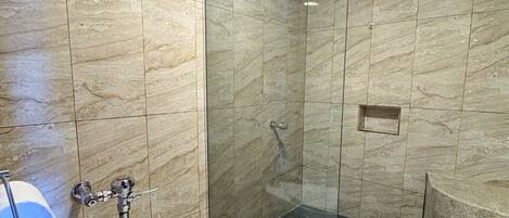 A bathroom with a toilet, a shower with glass doors, and a marble wall.