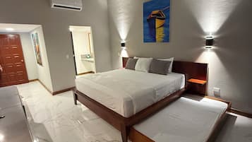 A bedroom with a large bed, a wooden headboard, and a nightstand with a lamp. There is a door and a painting on the wall.