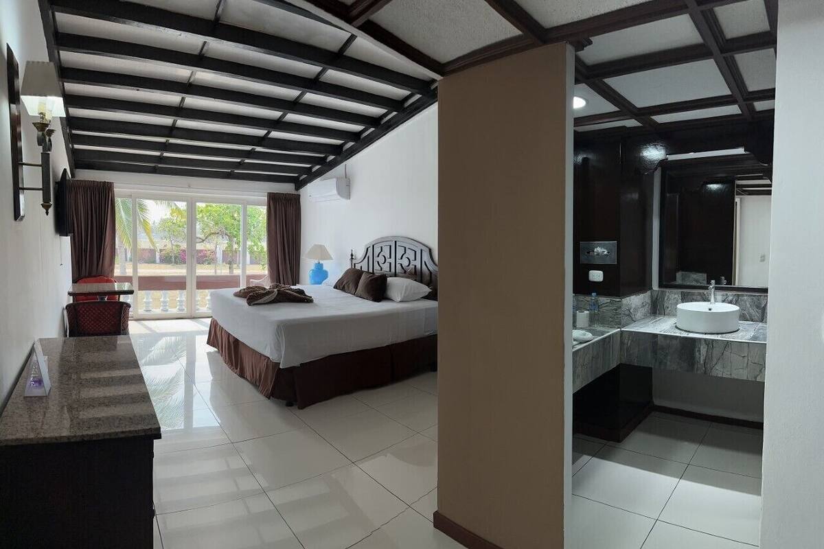 Ein Hotelzimmer mit Bett, Schreibtisch, Badezimmer mit Waschbecken und Spiegel sowie Blick ins Freie.