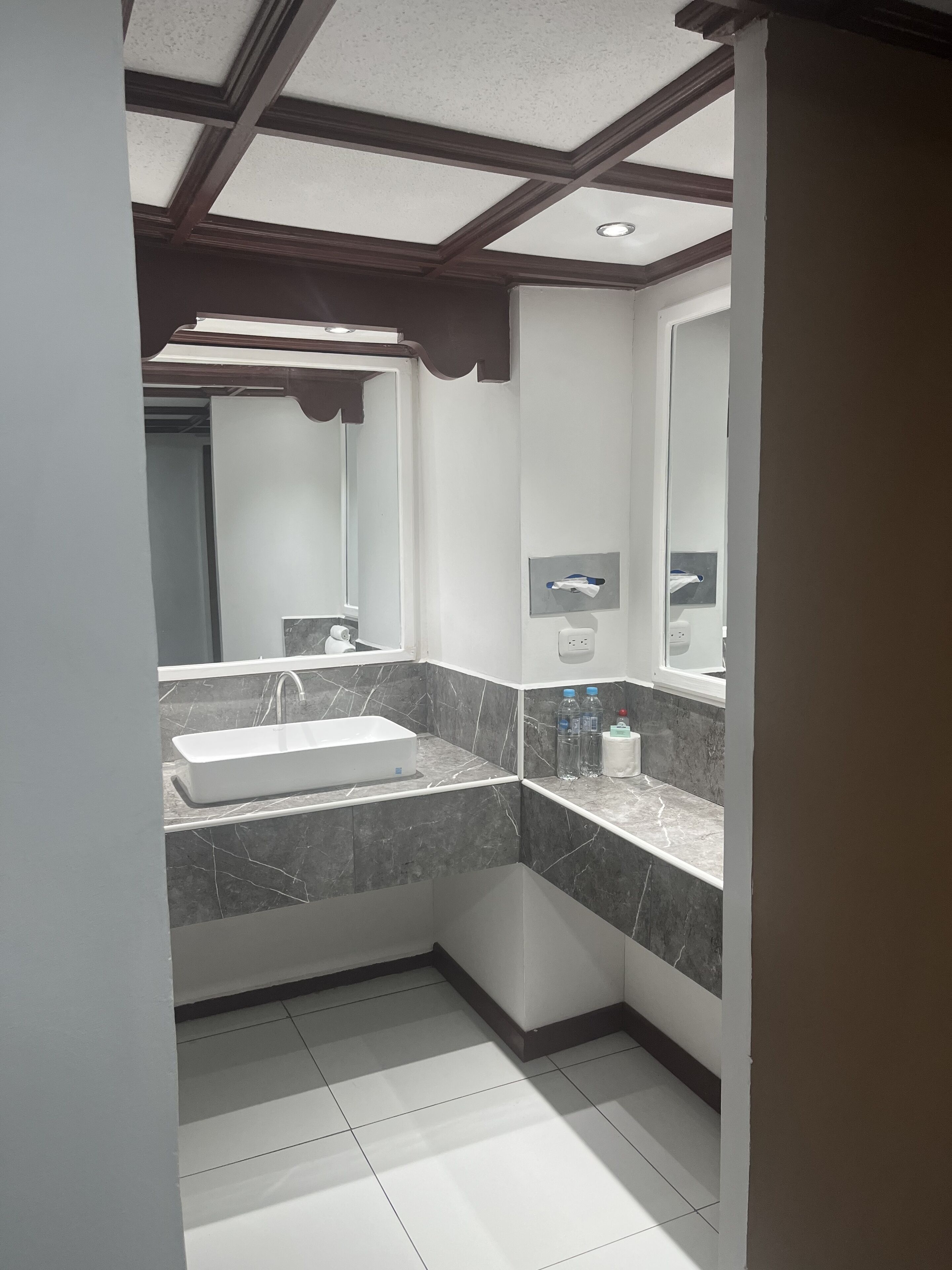 Casa de banho moderna com lavatório retangular, bancadas de mármore escuro e um espelho grande.