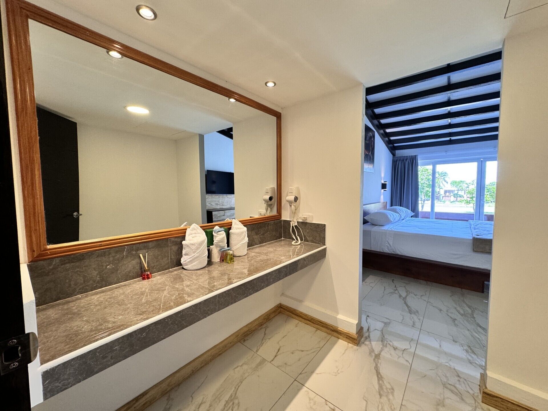 A modern bathroom with a large mirror, marble countertop, and a bed with a view.