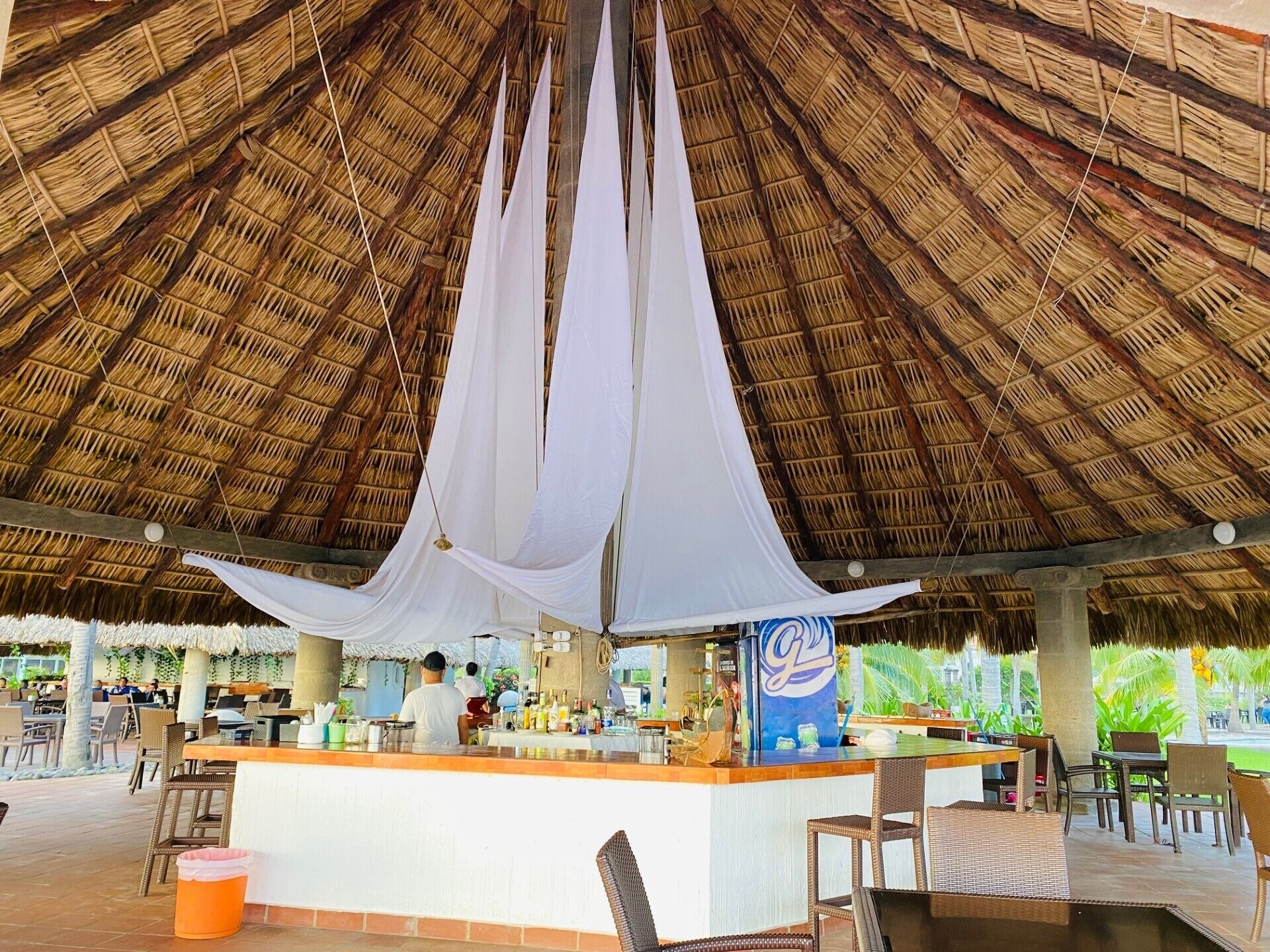 Zona de bar al aire libre con techo de paja, mostrador y asientos.
