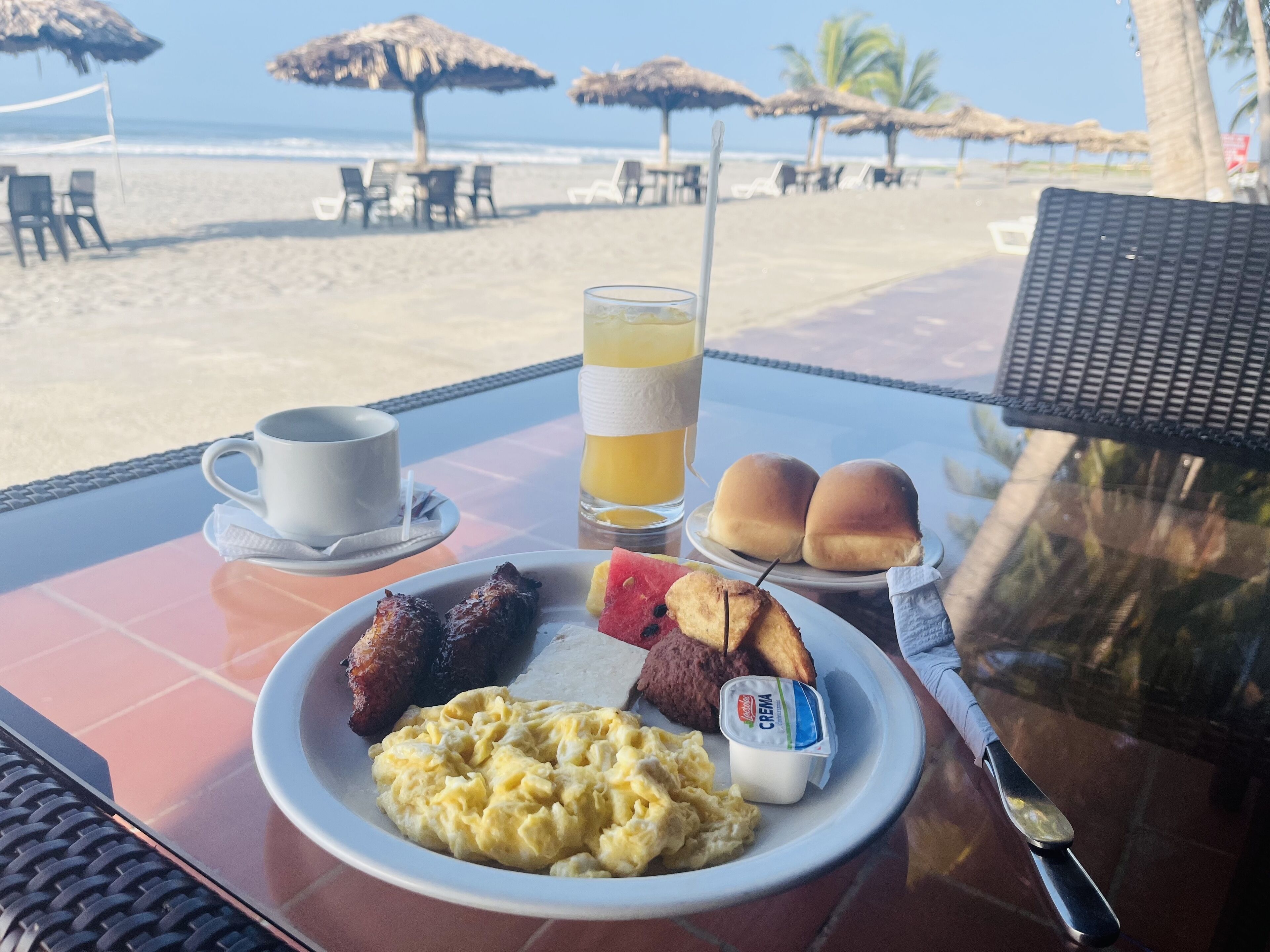 A breakfast table with a plate of food, a cup, a glass of juice, and a bottle of yogurt.