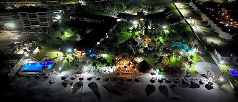 Vista aérea de un resort con varias piscinas, un edificio central imponente y palmeras circundantes.