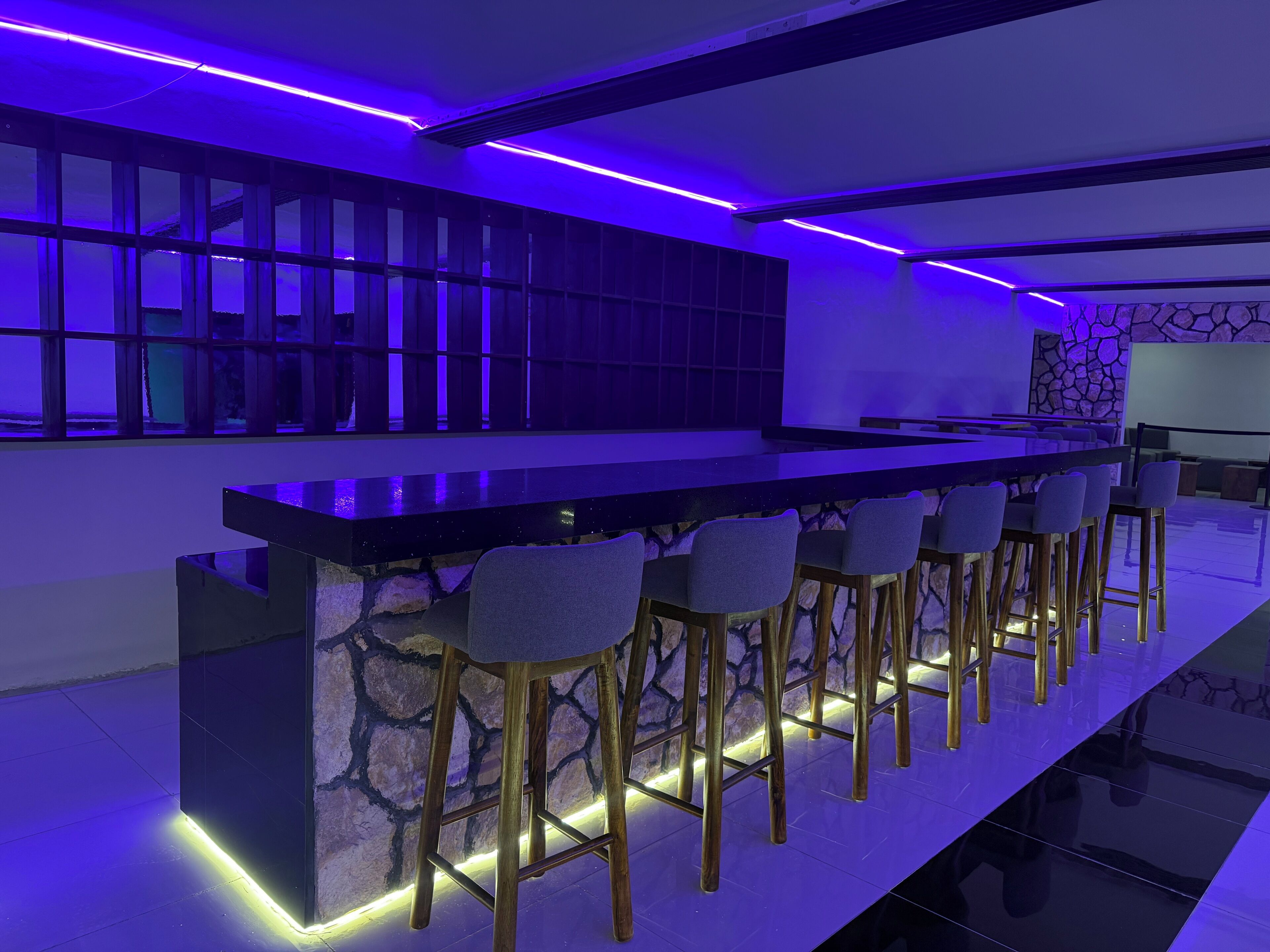 Un área de bar moderna con una barra alargada, taburetes y una pared de acento de piedra.