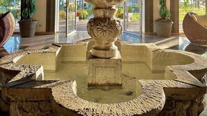 A stone fountain with water spouting from its center, surrounded by stone benches and potted plants. - HOTEL TESORO BEACH (La Herradura)