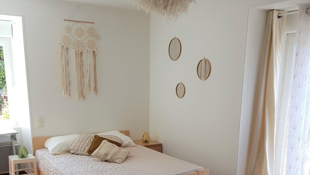 Une chambre avec un lit en bois, un tapis tissé et des éléments de décoration murale, notamment des miroirs ronds et une œuvre en macramé.