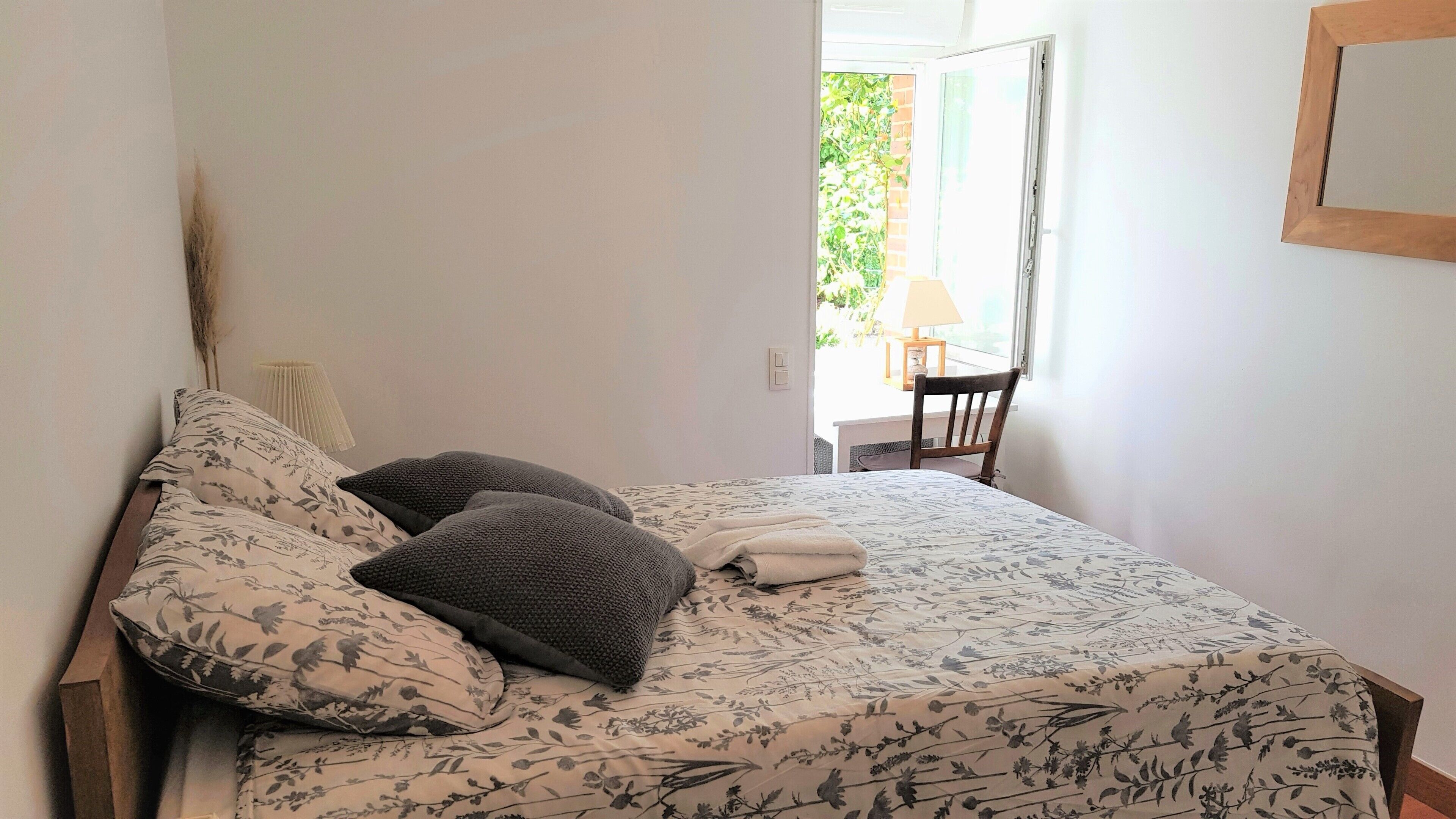 A bedroom with a bed, pillows, a bedside table, a lamp, and a chair.