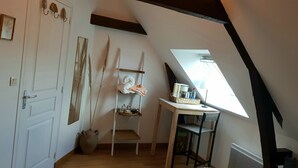 Une chambre située sous les combles, avec un plafond en pente, une petite table sur laquelle se trouve un panier, une étagère avec des serviettes et une porte dotée d’un miroir.