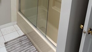 Un baño moderno con cabina de ducha de vidrio, un perchero y una alfombra pequeña en el suelo.