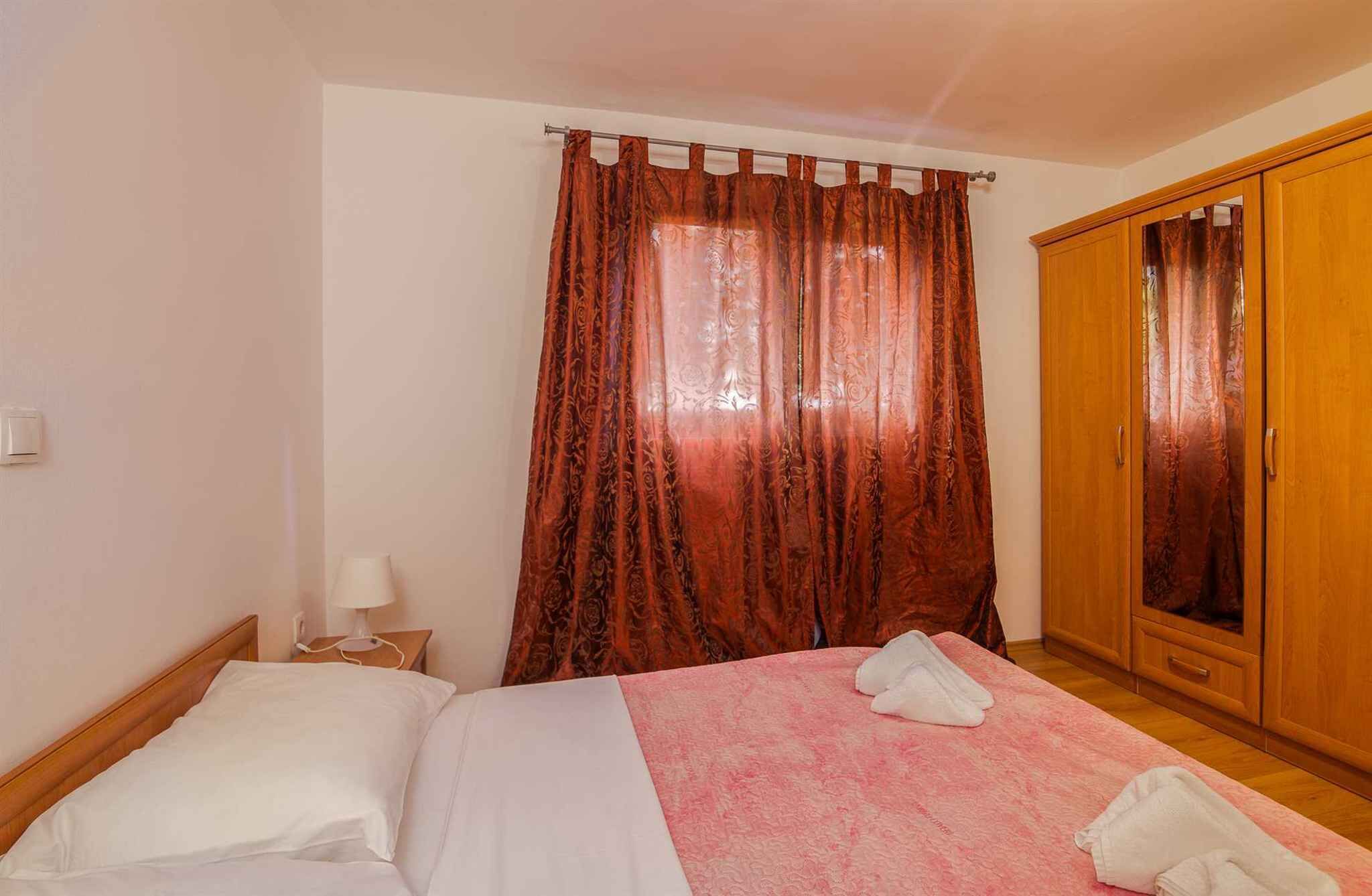 A bedroom with a bed, a nightstand, a lamp, a wardrobe, and a window with curtains.