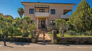 A two-story building with a central entrance, a balcony on the upper floor, and a stone wall surrounding the property. - Holiday apartment in the center of Njivice (Njivice)