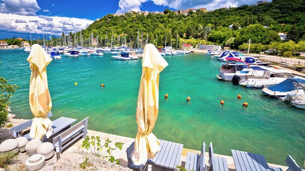 A marina with boats, a wooden deck with chairs and umbrellas, and a hillside with buildings in the background. - Holiday apartment in the center of Njivice (Njivice)