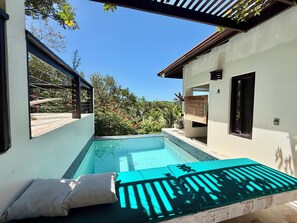 Una piscina con borde de cristal, una pérgola y vistas a exuberante vegetación.