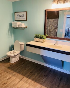 A bathroom with a toilet, sink, and a framed sign above the sink.