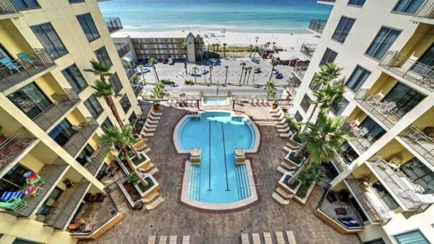 Ein Hotel mit einem zentral gelegenen Pool, umgeben von Liegestühlen, Balkonen und Blick auf den Strand.