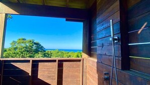 A wooden cabin with a large window overlooking a forest and ocean. - Havana Palms, 2 Bedroom Paradise (Milton Bight)