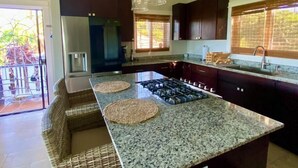 A modern kitchen with dark cabinets, a granite countertop, a central island, and pendant lighting. - Havana Palms, 2 Bedroom Paradise (Milton Bight)