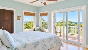 Un dormitorio con cama, una silla, ventilador de techo y vistas al exterior a través de amplias puertas correderas.