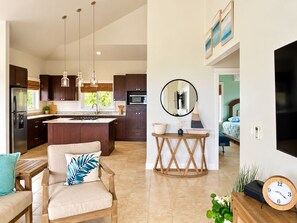 A modern kitchen with dark wood cabinets, a central island, pendant lights, and a dining area with a wooden table and a chair.