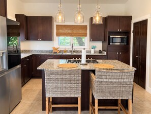Una cocina moderna con armarios de madera oscura, una isla central con taburetes, microondas integrado e iluminación colgante.