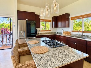 Una cocina moderna con una isla central, armarios de madera oscura, electrodomésticos de acero inoxidable y vistas a zonas verdes.