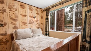 Une chambre à coucher avec une tête de lit en bois, un grand lit recouvert d’une courtepointe beige et une fenêtre avec des rideaux.