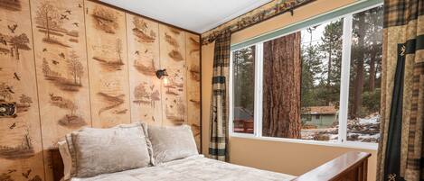 Une chambre à coucher avec une tête de lit en bois, un grand lit recouvert d’une courtepointe beige et une fenêtre avec des rideaux.