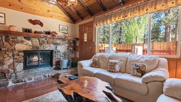 Un salon chaleureux avec une cheminée en pierre, un plafond en bois et une grande fenêtre donnant sur les arbres.