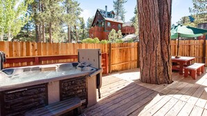 Une terrasse en bois avec un jacuzzi, une table de pique-nique et un grand arbre.
