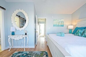 A bedroom with a bed, a mirror, a bedside table, a lamp, and a painting on the wall.