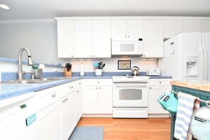 A modern kitchen with white cabinets, a stainless steel sink, a microwave, an oven, and a refrigerator.