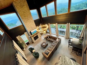 A spacious living area with a fireplace, large windows, and a view of the mountains.