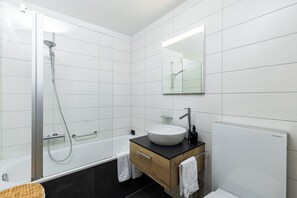 Ett modernt badrum med en dusch som är avskärmad med glasväggar, en vit handfat och en spegel ovanför tvättstället.
