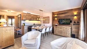 Una cocina moderna con armarios de madera, una zona de comedor con sillas blancas y un televisor montado en una pared de madera.
