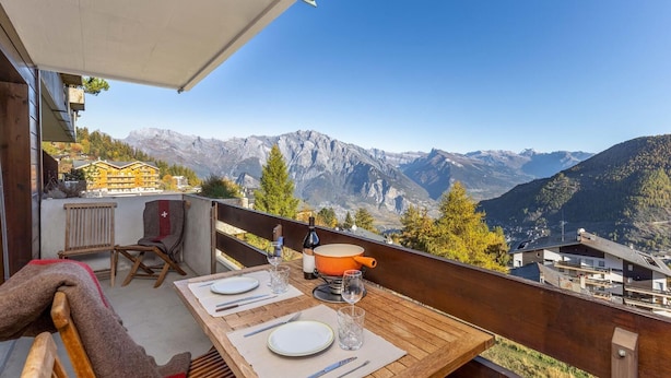 Una mesa de madera dispuesta para comer, con vistas a la montaña, una silla y una lámpara de mesa pequeña.