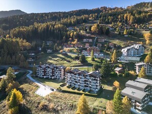 A residential area with multiple apartment buildings, surrounded by forested hills and a clear sky. - Apartment La Foret (Riddes)