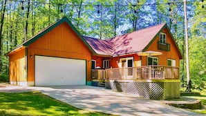 A two-story wooden house with a garage, a balcony with outdoor furniture, and a well-maintained lawn. - Higgins Lake Retreat - Hike, Swim, Relax! (Roscommon)