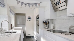 Eine moderne Küche mit weißen Schränken, einer zentralen Kochinsel, einem eingebauten Backofen und einer Edelstahl-Dunstabzugshaube.