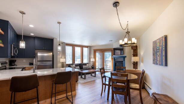 A modern kitchen with a large island, dark cabinets, stainless steel appliances, and a dining area with wooden furniture.