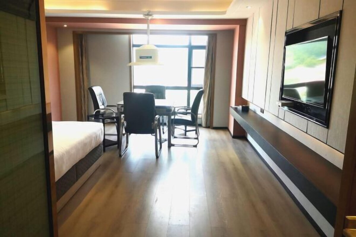 A hotel room with a bed, a desk, two chairs, a TV, and a window with curtains.
