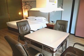 A hotel room with a bed, two chairs, a table, and a lamp.