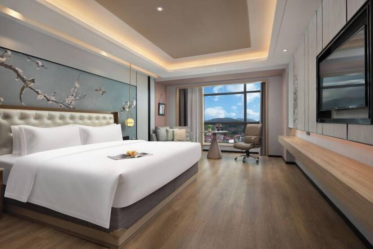 A modern hotel room with a large bed, a TV mounted on the wall, and a view of the mountains through the window.