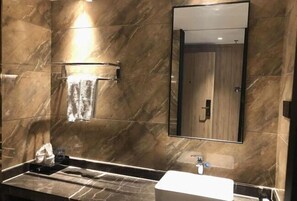 A modern bathroom with a marble wall, a large mirror, and a sink.