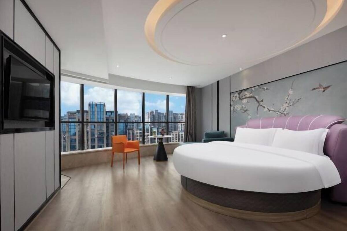 A modern hotel room with a large bed, a city view, a television, and a dining area.