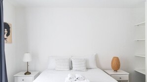 A minimalist hotel room with a bed, two bedside tables, a lamp, a vase, and a painting on the wall. - The City Song 1 bedroom apartment in Rotherhithe (London)