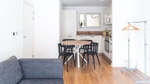 A modern kitchen with white cabinets, a wooden dining table, and black chairs. - The City Song 1 bedroom apartment in Rotherhithe (London)