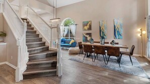 A spacious living area with a staircase, a dining table with chairs, and artwork on the walls. - Luminous Home w/ Pool, Spa & Game Lounge (Round Rock)