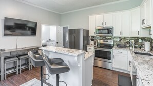 Een moderne keuken met witte kasten, roestvrijstalen apparatuur, een marmeren eiland en een flatscreen televisie.
