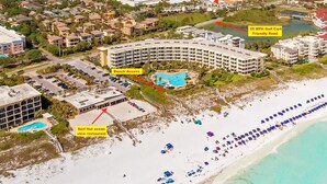 An aerial view of a coastal resort with a pool, beach access, a surf hut ocean view restaurant, and a golf cart friendly road.